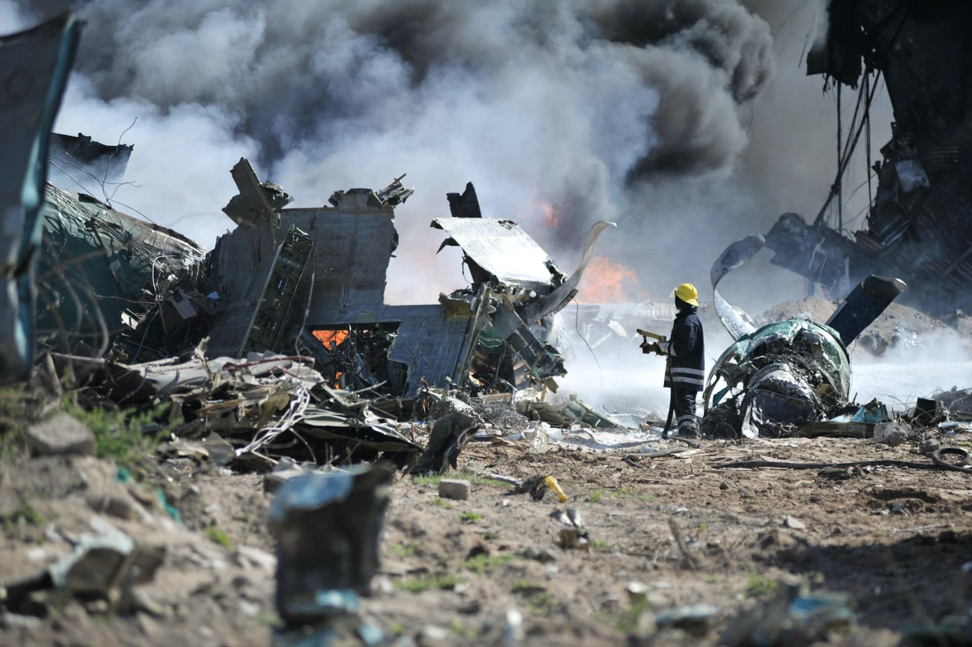 A firefighter stands by a smoldering aircraft wreck.